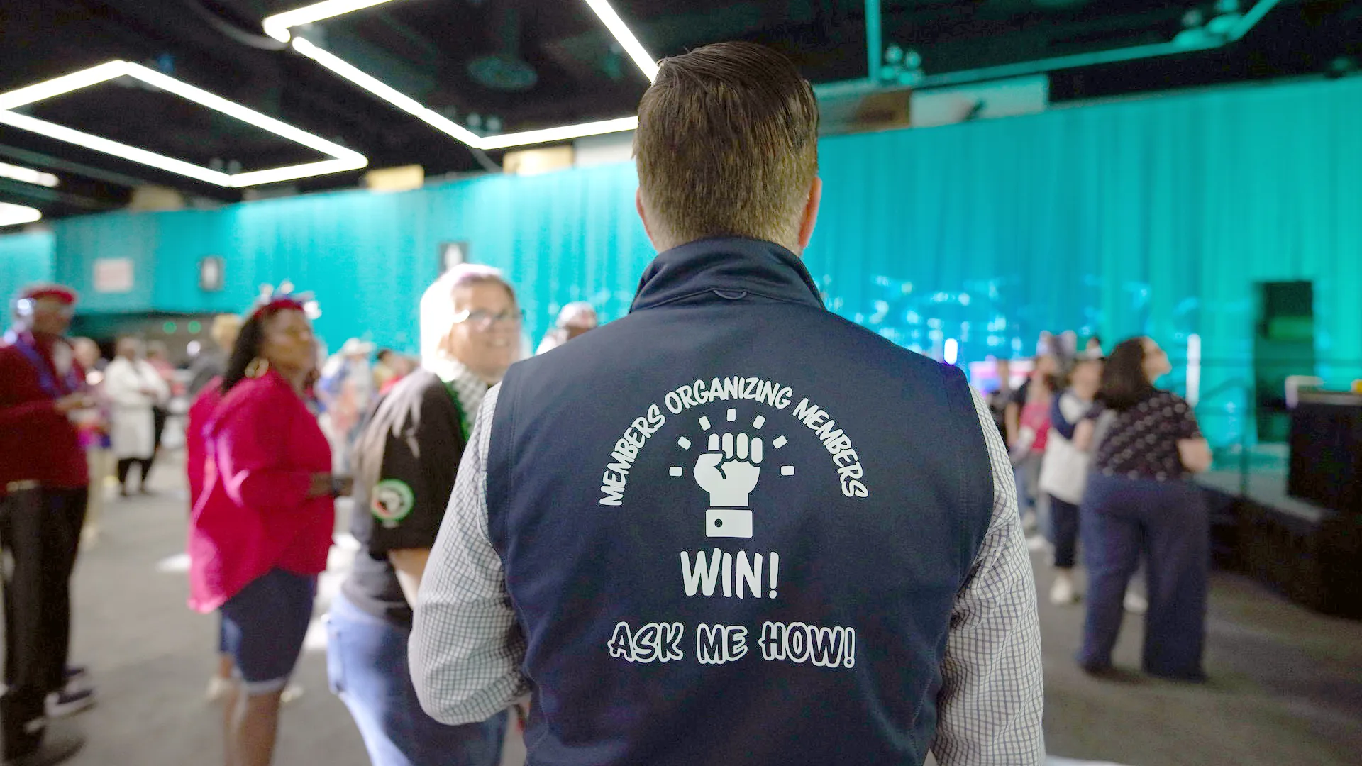 A man wearing a blue vest that reads "Members Organizing Members Win! Ask Me How!"