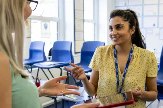 Educators stand in classroom talking over an iPad