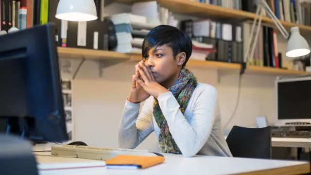 young female teacher sitting at desk and reading on a desktop computer