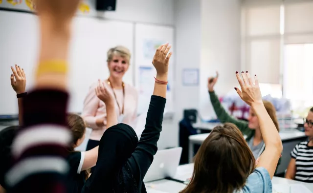 Teacher stands in front of classroom and calls on students with raised hands